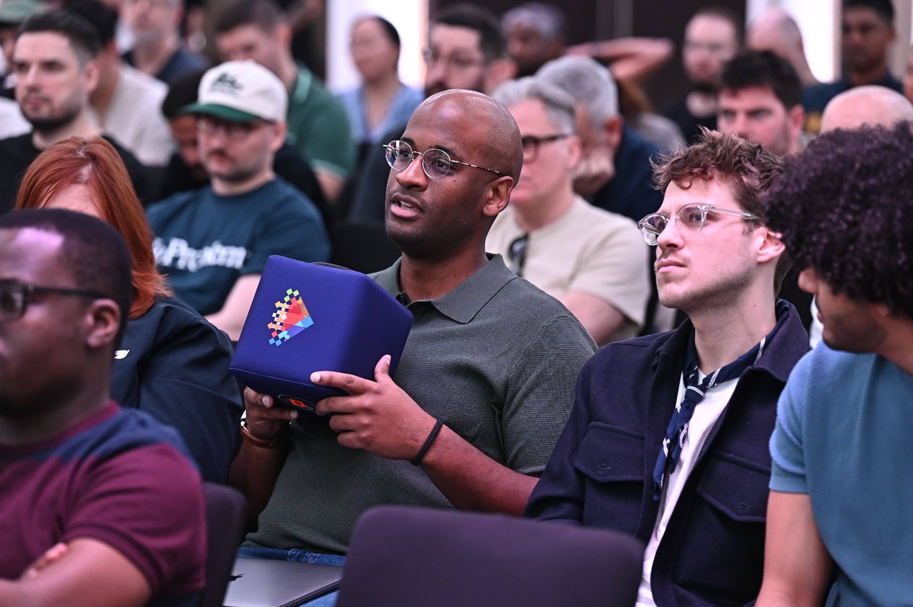 A diverse group of individuals attentively listen in a crowded conference room.